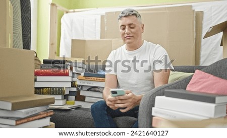 Young caucasian man using smartphone sitting on sofa at new home
