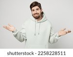 Young caucasian man wear mint hoody shrugging shoulders looking puzzled, have no idea, nothing to say spread hands isolated on plain solid white background studio portrait. People lifestyle concept