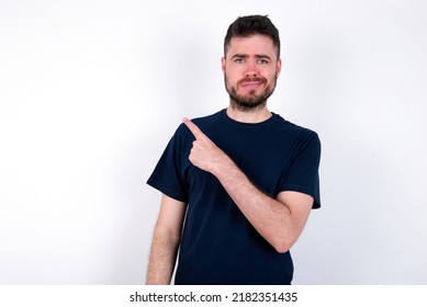 Young Caucasian Man Wearing Black T-shirt Over White Background Pointing Aside Worried And Nervous With Forefinger, Concern And Surprise Concept.