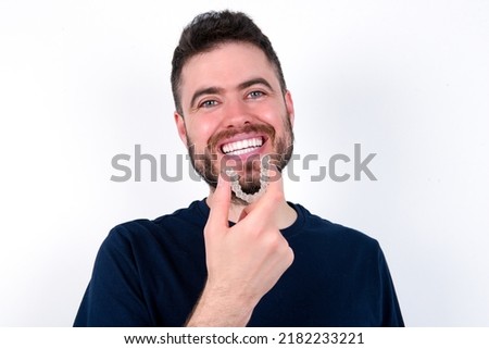 Young caucasian man wearing black T-shirt over white background holding an invisible aligner ready to use it. Dental healthcare and confidence concept.
