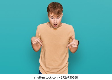 Young caucasian man wearing casual clothes pointing down with fingers showing advertisement, surprised face and open mouth 