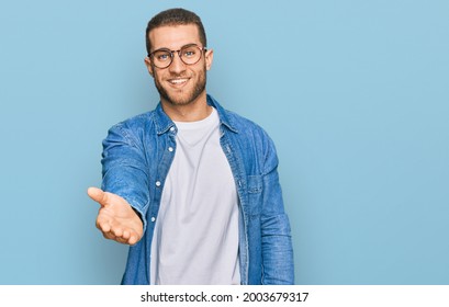 Young caucasian man wearing casual clothes smiling cheerful offering palm hand giving assistance and acceptance.  - Shutterstock ID 2003679317