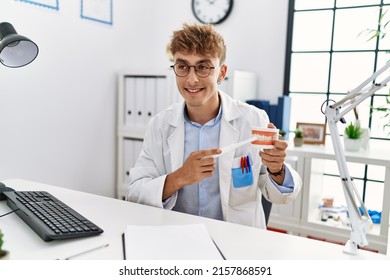 Young Caucasian Man Wearing Dentist Uniform Cleaning Denture Using Toothbrush At Clinic