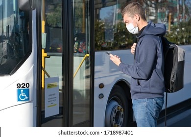 Young Caucasian Man Wearing Face Mask And Looking At Mobile While Taking The Bus During Pandemic Covid-19. Health And Care Concept