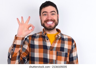 young caucasian man wearing plaid shirt over white background hold hand arm okey symbol toothy approve advising novelty news