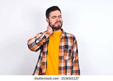 Young Caucasian Man Wearing Plaid Shirt Over White Background Suffering From Back And Neck Ache Injury, Touching Neck With Hand, Muscular Pain.