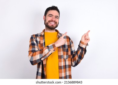 young caucasian man wearing plaid shirt over white background with positive expression, indicates with fore finger at blank copy space for your promotional text or advertisement.