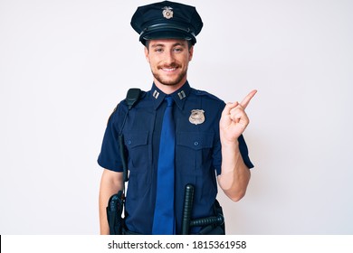 Young Caucasian Man Wearing Police Uniform With A Big Smile On Face, Pointing With Hand Finger To The Side Looking At The Camera. 