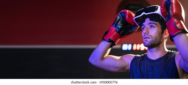 Young caucasian man wearing red boxing gloves and using glasses of virtual reality in sport gym.Smartphone using with VR headset,future technology concept.Man using VR glasses in colorful neon lights.
