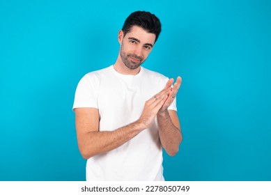 Young caucasian man wearing white T-shirt over blue background clapping and applauding happy and joyful, smiling proud hands together. - Shutterstock ID 2278050749