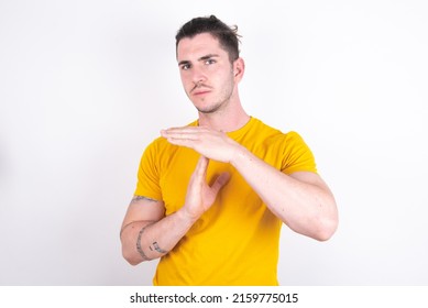 Young caucasian man wearing yellow t-shirt over white background feels tired and bored, making a timeout gesture, needs to stop because of work stress, time concept.