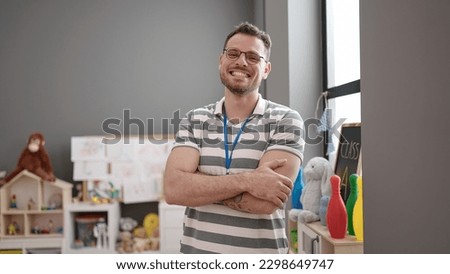 Young caucasian man working as teacher smiling with crossed arms at kindergarten