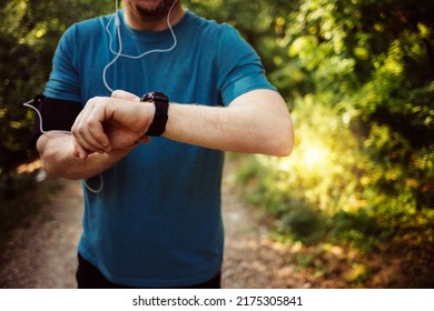 Young Caucasian Men Using Smart Watch Measuring Heart Rate During Walk. Runner Fixing Time At Sports Smart Watch. Young Athletic Man Using Fitness Tracker Or Smart Watch Before Run Training Outdoors.