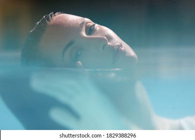 Young Caucasian Model Posing In Turquoise Water At SPA And Looking At Camera. Half Underwater View Of Beautiful Girl Relaxing In Pool. 