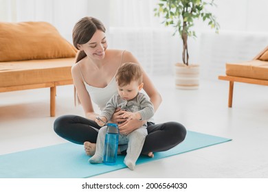 Young caucasian mother doing fitness exercises after labor and baby delivery on mat, meditating with her little toddler son infant baby at home on lockdown. Shaping body in postnatal period