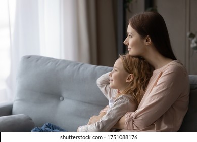 Junge kaukasische Mutter und kleine Vorschultochter entspannen sich auf dem Sofa in der Ferne, die zusammen träumen, träumen Mutter und kleine Mädchen Umarmung kuscheln, träumen oder visualisieren auf dem Sofa im Wohnzimmer
