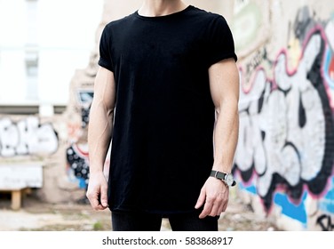 Young Caucasian Muscular Man Wearing Black Tshirt And Jeans Posing In Modern District.Blurred Graffiti On The Background. Hotizontal Mockup