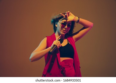 Young Caucasian Musician, Performer Singing On Gradient Background In Neon Light. Concept Of Music, Hobby, Festival. Joyful Woman Party Host, DJ, Singer, Band's Front Artist. Colorful Portrait.