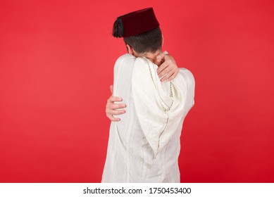 Young Caucasian Muslim Man Wearing Djellaba And Traditional Hat Over Red Background Hugging Herself Happy And Positive From Backwards. Self Love And Self Care