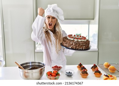 Young caucasian pastry chef woman cooking pastries and cake at the kitchen annoyed and frustrated shouting with anger, yelling crazy with anger and hand raised 