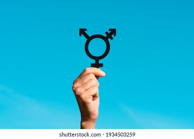 a young caucasian person holds a transgender symbol against the blue sky, with some blank space around