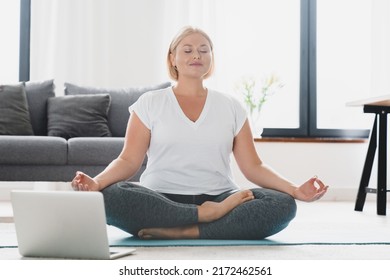 Young Caucasian Plump Plus Size Fat Girl Athlete Woman In Sporty Clothes Doing Training Workout Yoga At Home, Meditating In Lotus Position Using Laptop On Online Tutorial