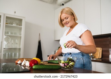 Young caucasian plump plus size woman cooking making salad, healthy food, dieting, counting calories, preparing dinner lunch at home kitchen - Powered by Shutterstock