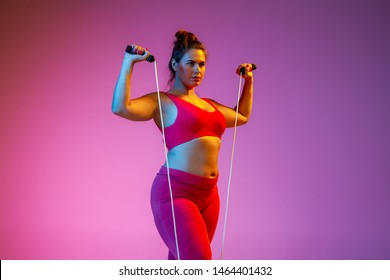 Young Caucasian Plus Size Female Model's Training On Gradient Purple Background In Neon Light. Doing Workout Exercises With The Jump Rope. Concept Of Sport, Healthy Lifestyle, Body Positive, Equality.