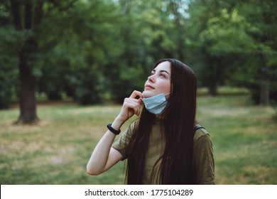 Young caucasian pretty woman removes a medical protective mask from her face on nature, surrounded by trees, breathing clean fresh air - Powered by Shutterstock