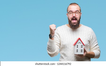 Young Caucasian Real State Agent Man Holding House Isolated Background Screaming Proud And Celebrating Victory And Success Very Excited, Cheering Emotion