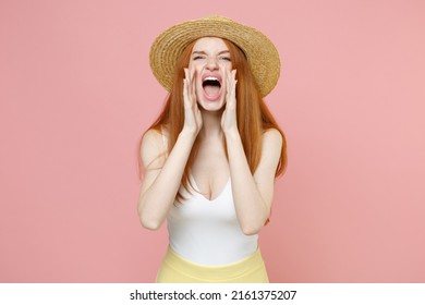 Young caucasian redhead woman 20s ginger long hair wearing straw hat and summer clothes shouting screaming news with hands arms near mouth isolated on pastel pink color background studio portrait.