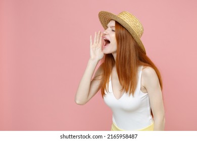 Young caucasian redhead woman 20s ginger long hair wearing straw hat and summer clothes shouting aside screaming news with hands arms near mouth isolated on pastel pink background studio portrait.