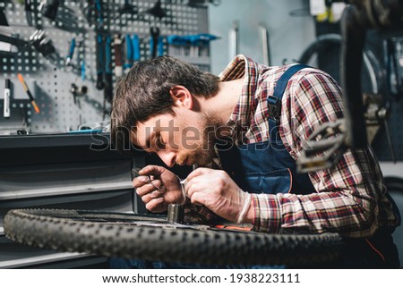 Young caucasian repairman repairing mountain bike wheel in bike shop workshop. Fixing bicycle. Caring for you wheels. man mechanic working in garage. Worker fixing cycle gear. Small business theme.