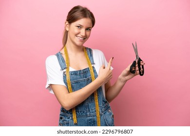 Young caucasian seamstress woman isolated on pink background pointing back