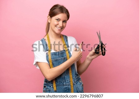 Young caucasian seamstress woman isolated on pink background pointing back