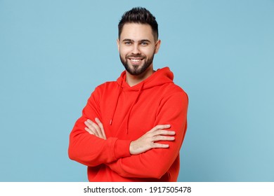 Young Caucasian Smiling Happy Bearded Attractive Handsome Student Man 20s Wear Casual Red Orange Hoodie Hold Hands Crossed Folded Isolated On Blue Background Studio Portrait People Lifestyle Concept