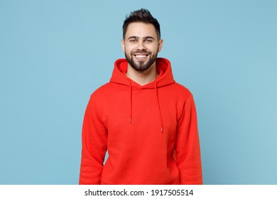 Young caucasian smiling happy cheerful bearded attractive handsome student man 20s wearing casual red orange hoodie looking camera isolated on blue background studio portrait People lifestyle concept