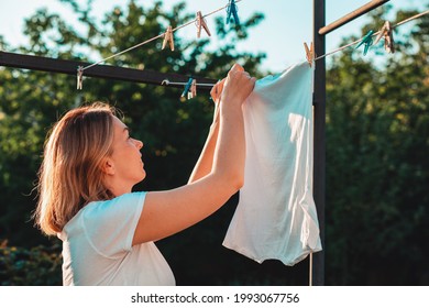 Una joven caucásica esposa sonriente colgando de la ropa. Vertical. Concepto de trabajo doméstico.
