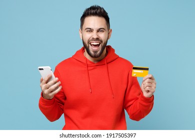 Young caucasian smiling overjoyed excited bearded man 20s wearing casual red orange hoodie hold mobile cell phone credit bank card isolated on blue background studio portrait Online shopping concept - Powered by Shutterstock