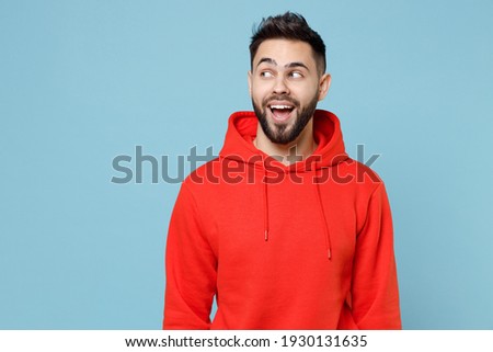 Young caucasian smiling pensive wistful dreamful happy bearded attractive man 20s wearing casual red orange hoodie looking aside isolated on blue background studio portrait People lifestyle concept