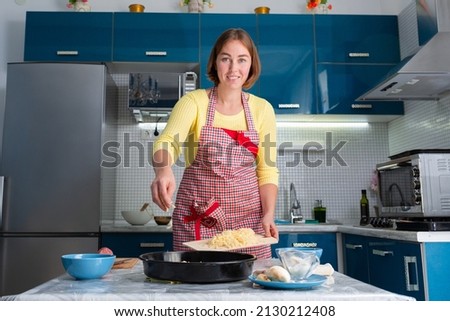 Young Caucasian smiling woman in an apron preparing a home cooked meal. The kitchen is in the background. The concept of homemade food.