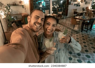 A young Caucasian and Spanish couple are taking a selfie while drinking a gin tonic in a bar. Concept of leisure romantic activities - Powered by Shutterstock