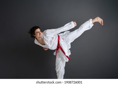 Young caucasian sportsman dressed in kimono practice in karate isolated over gray background
