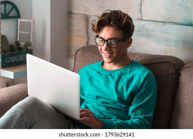 Young caucasian student study at home with internet and laptop computer sitting on the couch - home school concept - video conference and communicating people - happy boy