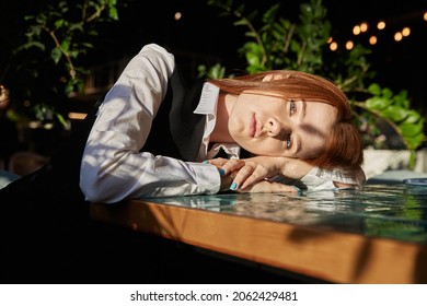 Young Caucasian Stylish Redhead Pretty Woman With Long Hair Lays Her Head On Table At Coffee Shop. Beautiful Pensive Melancholic Red Headed Lady Laying At Sunny Cafe, Having Rest. Lifestyle Portrait