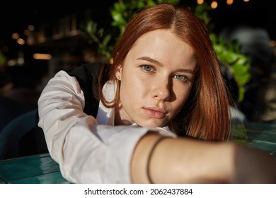 Young Caucasian Stylish Redhead Pretty Woman With Long Hair Lays Her Head On Her Arms And Table. Beautiful Pensive Melancholic Red Headed Lady Laying At Sunny Cafe. Lifestyle Portrait