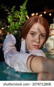 Young Caucasian Stylish Redhead Pretty Woman With Long Hair Lays Her Head On Her Arms And Table. Beautiful Pensive Melancholic Red Headed Lady Laying At Sunny Cafe. Lifestyle Portrait