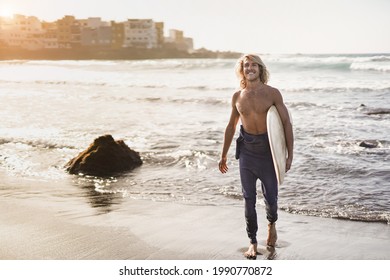 Young Caucasian Surfer Man Walking On The Beach With A Surfboard - Concept Of Extreme Sport And Healthy Lifestyle