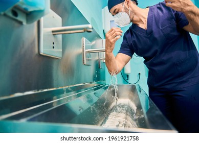 young Caucasian surgeon in scrubs washes his hands before entering the operating room in hospital. Focus on the face - Powered by Shutterstock