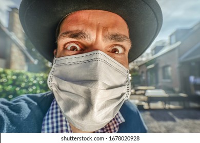 Young Caucasian survivalist man wearing white anti virus protective face mask and black hat against Covid-19 Coronavirus epidemic. Anxious looking man with eyes wide open during worldwide lockdown.